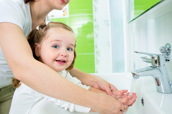 Mãe ajuda filha a lavar as mãos