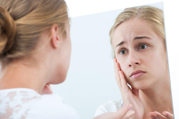 Mulher com ar preocupado vê-se ao espelho