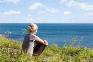 Mulher sentada em falésia a observar o mar