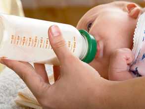 Mão a dar biberão de leite a bebé