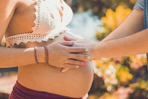 Grávida a segurar as mãos do marido na sua barriga