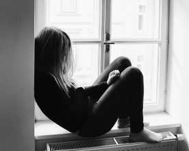 Adolescente sentada no parapeito interior da janela
